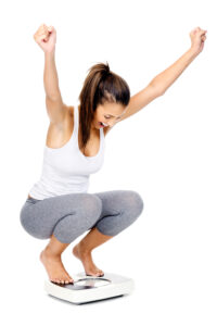 Young woman kneels on a bathroom scale and cheers at her weight loss with Semaglutide