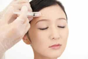 A young woman closes her eyes as her Botox injector treats wrinkles.