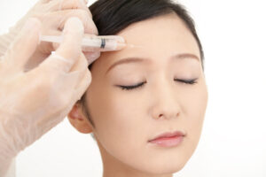 A young woman closes her eyes as her Botox injector treats wrinkles.