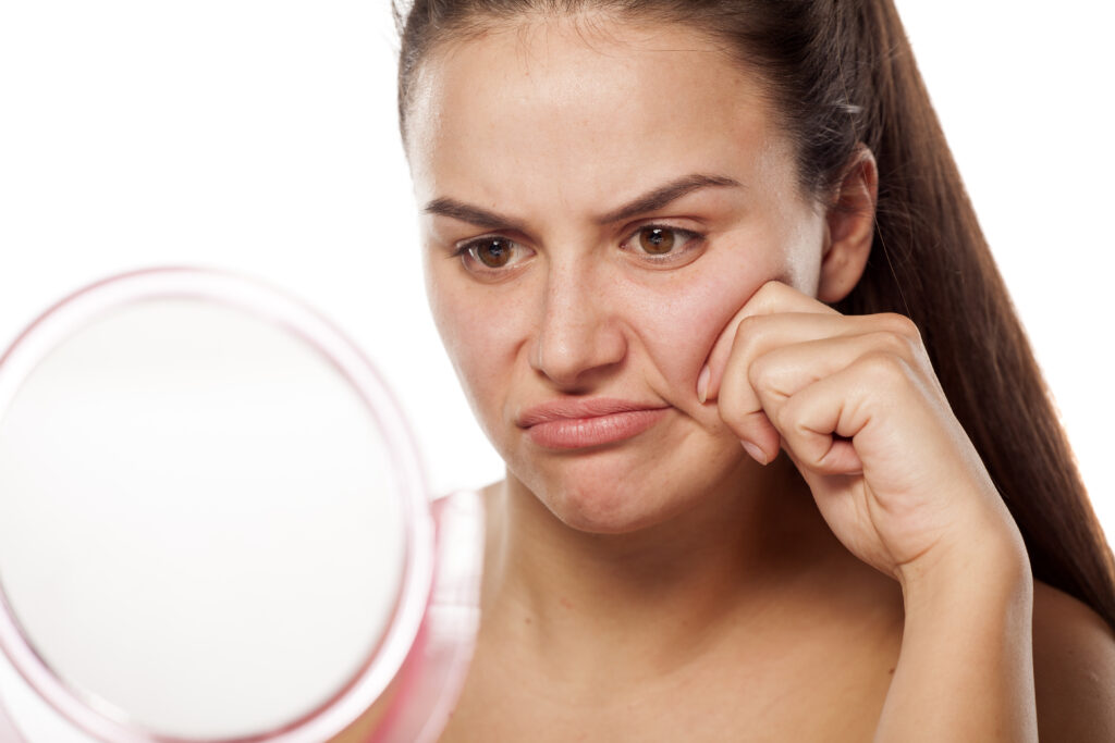 Attractive brunette woman pinches her cheek and frowns in the mirror in Salt Lake City, frustrated with her wrinkles